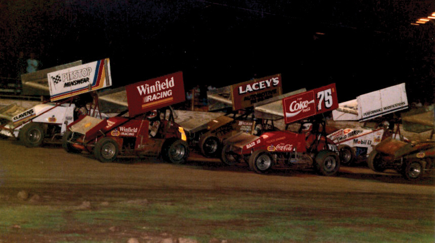 National Sprintcar Champion George Tatnell brings the field around for the start of a Winfield Sprintcar Series Lismore round event in the late 80s. Sharing the front row with Tatnell is Max Dumesny, while in the second row it's John Walsh (on the inside) and Brett Lacey.